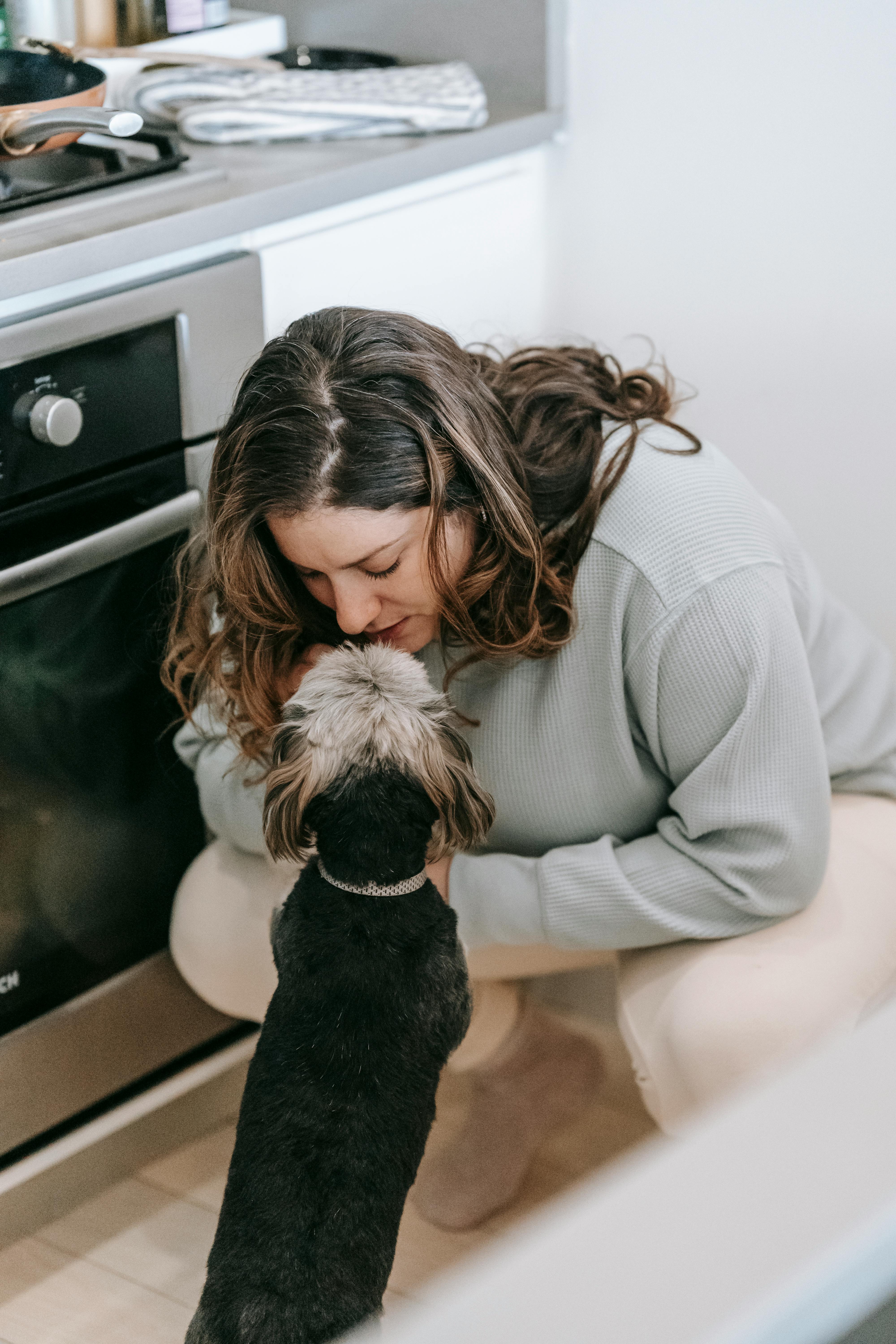 Woman Cuddling Small Dog In Kitchen