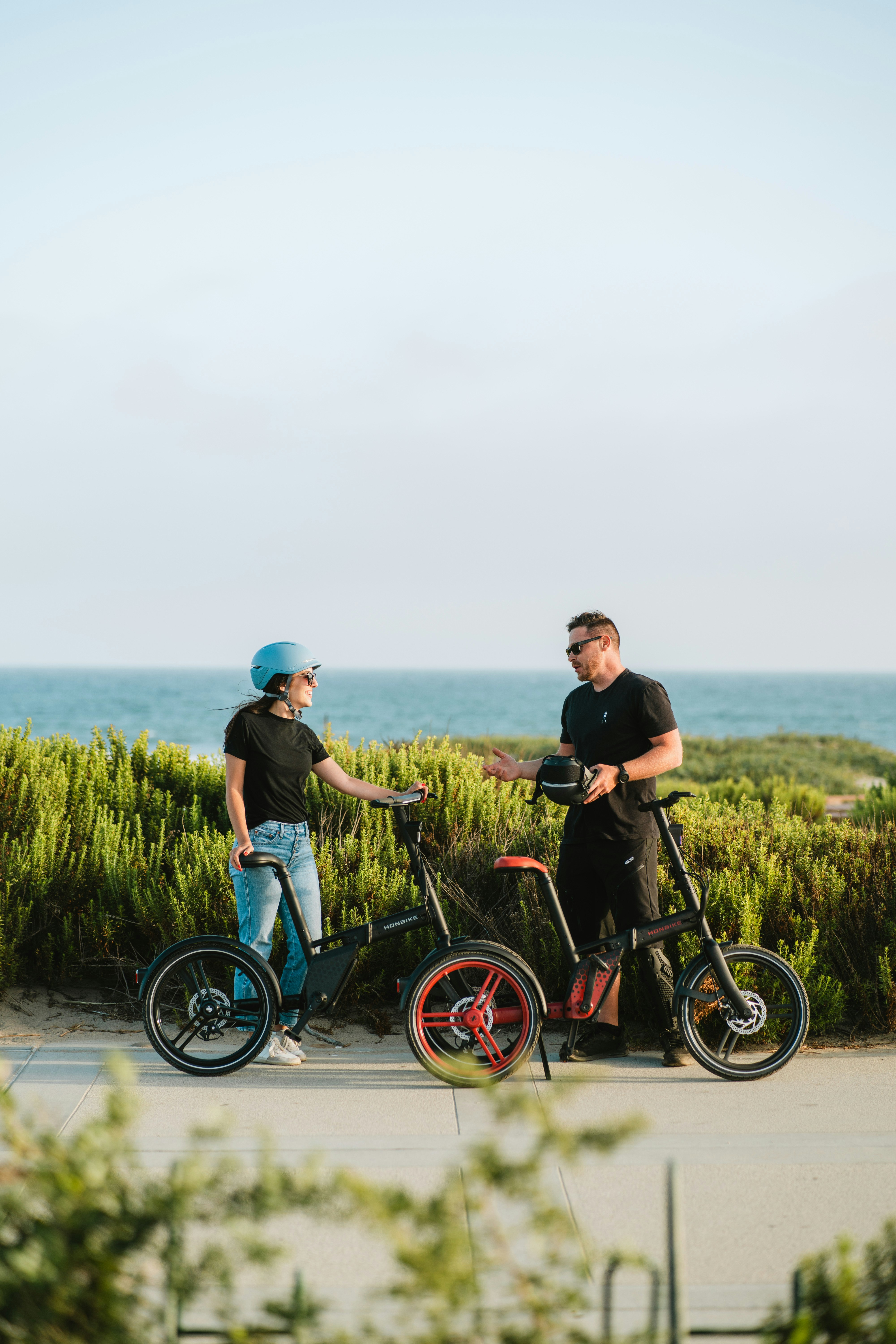 Two Cyclists Chatting By The Sea