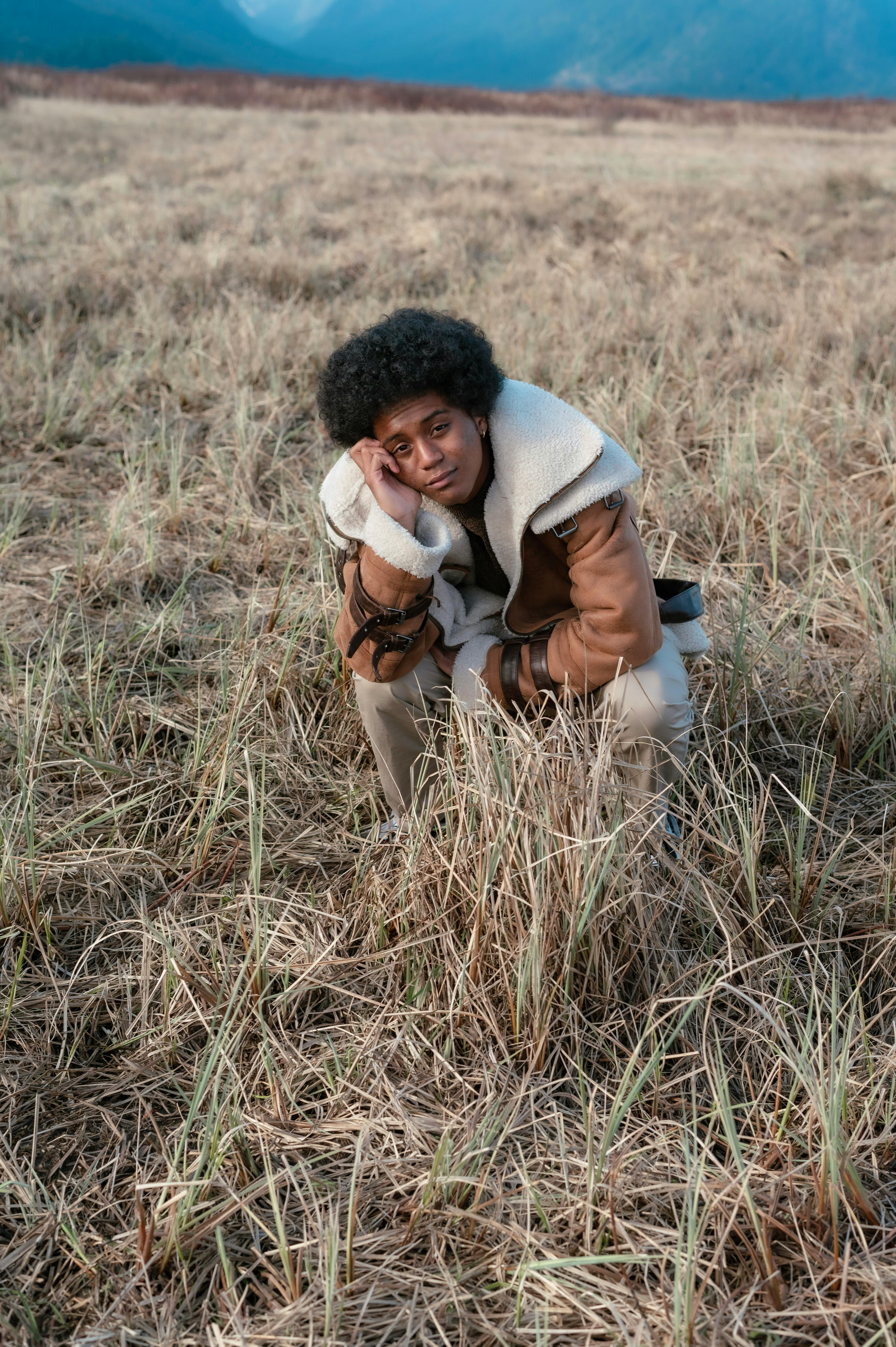 Person Crouching in Dry Grass Field