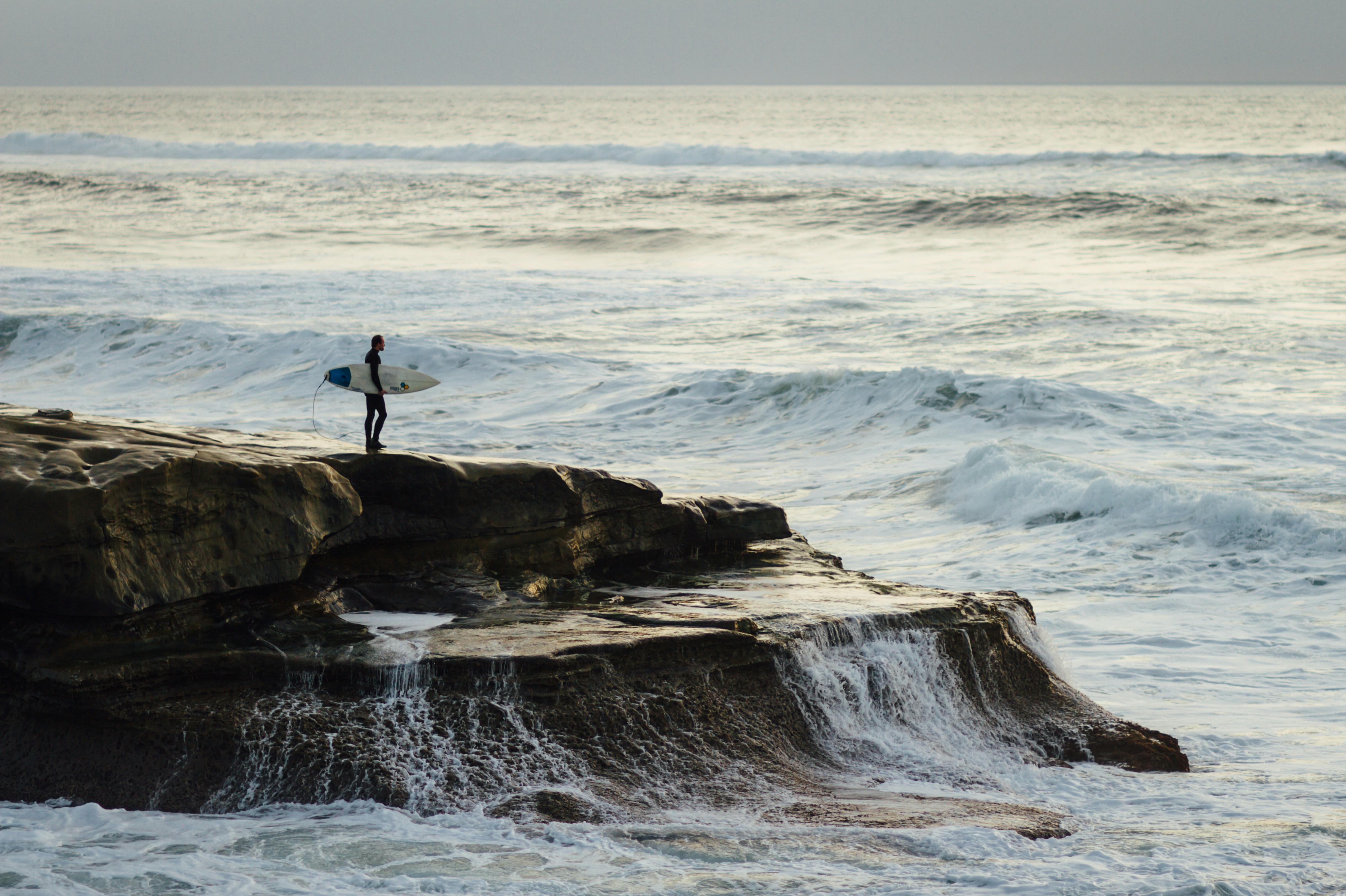 Surfer on Coastal Rock Facing Ocean