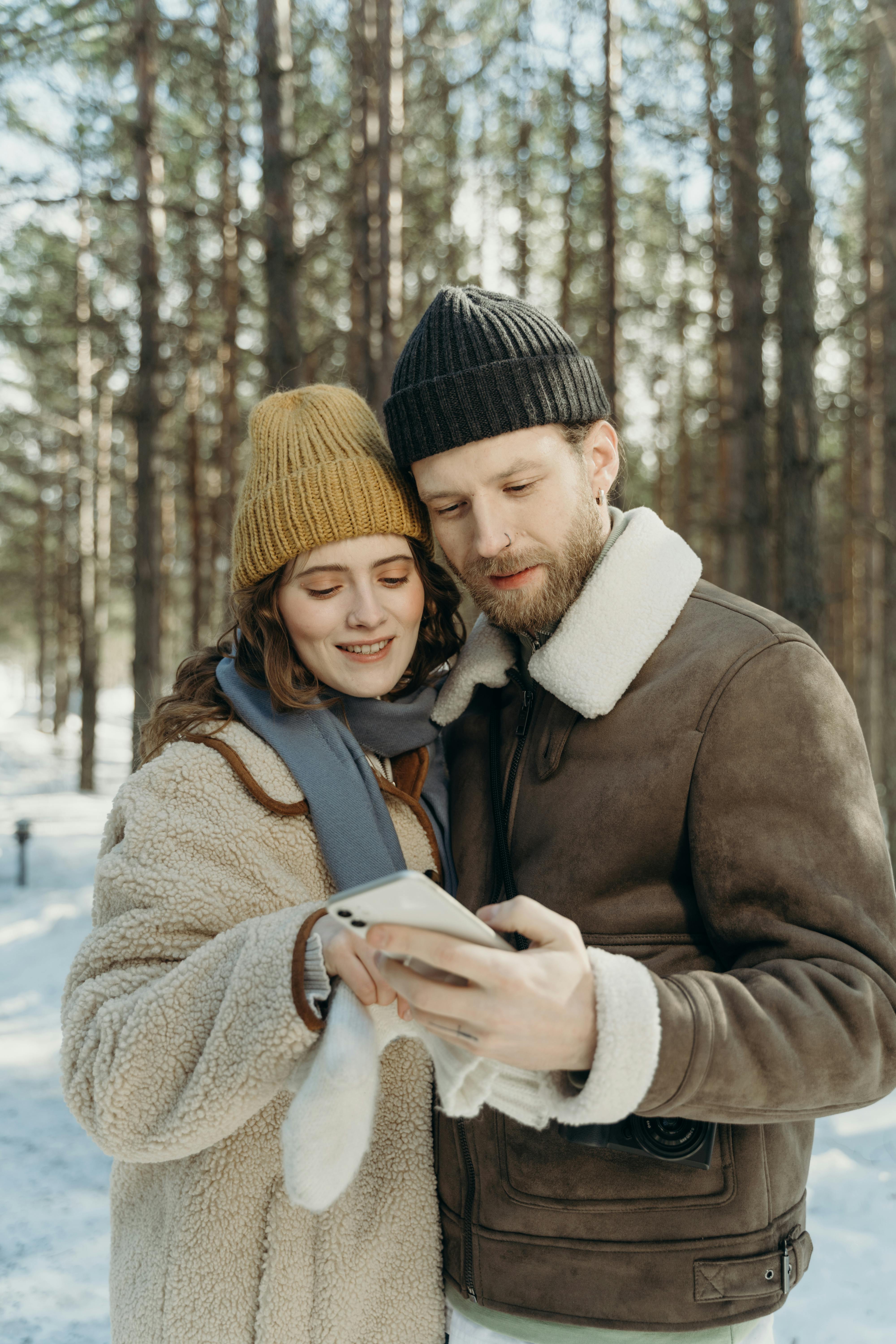 Couple Looking at Phone in Snowy Pine Forest