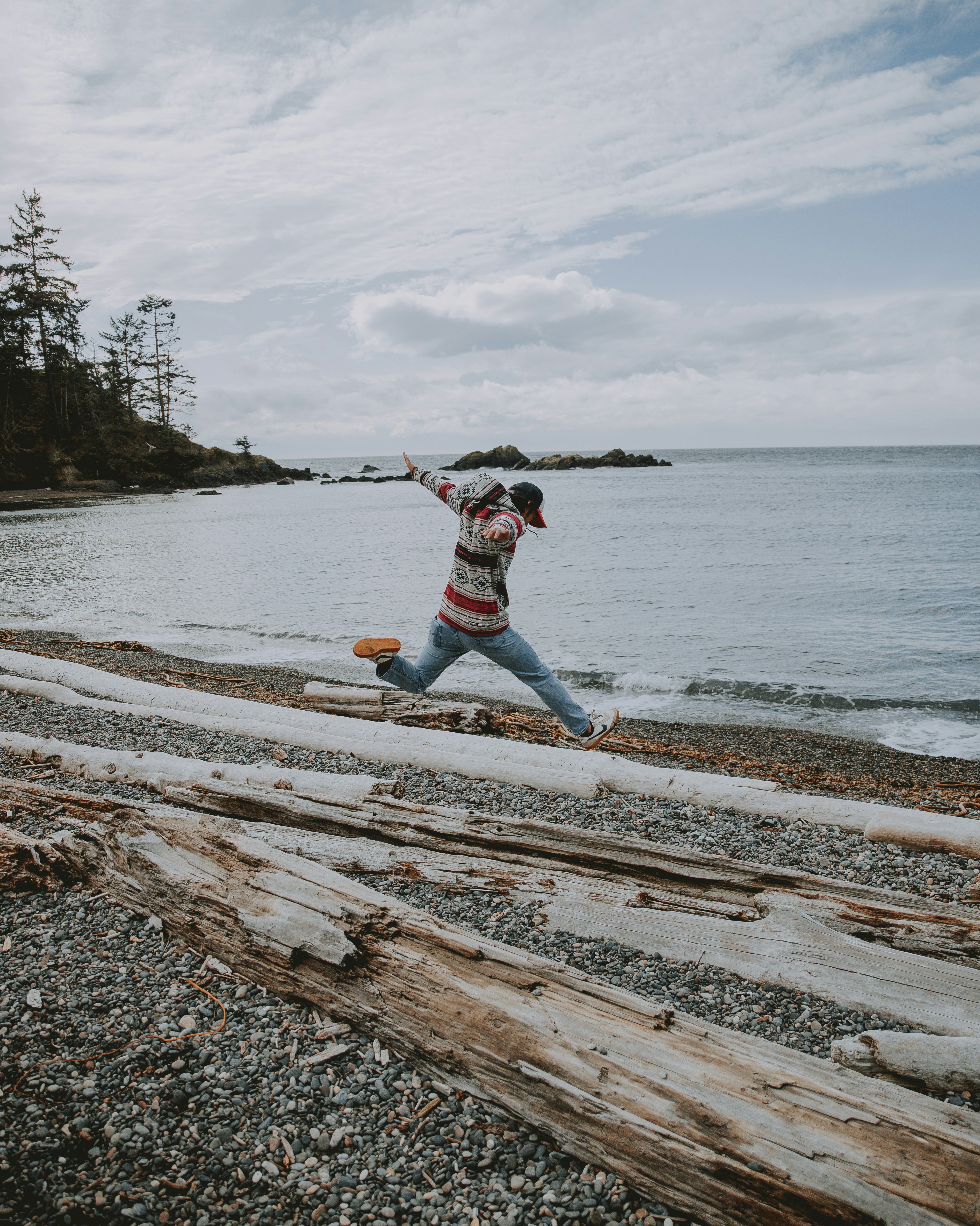 Person Jumps Over Driftwood on Seaside Beach
