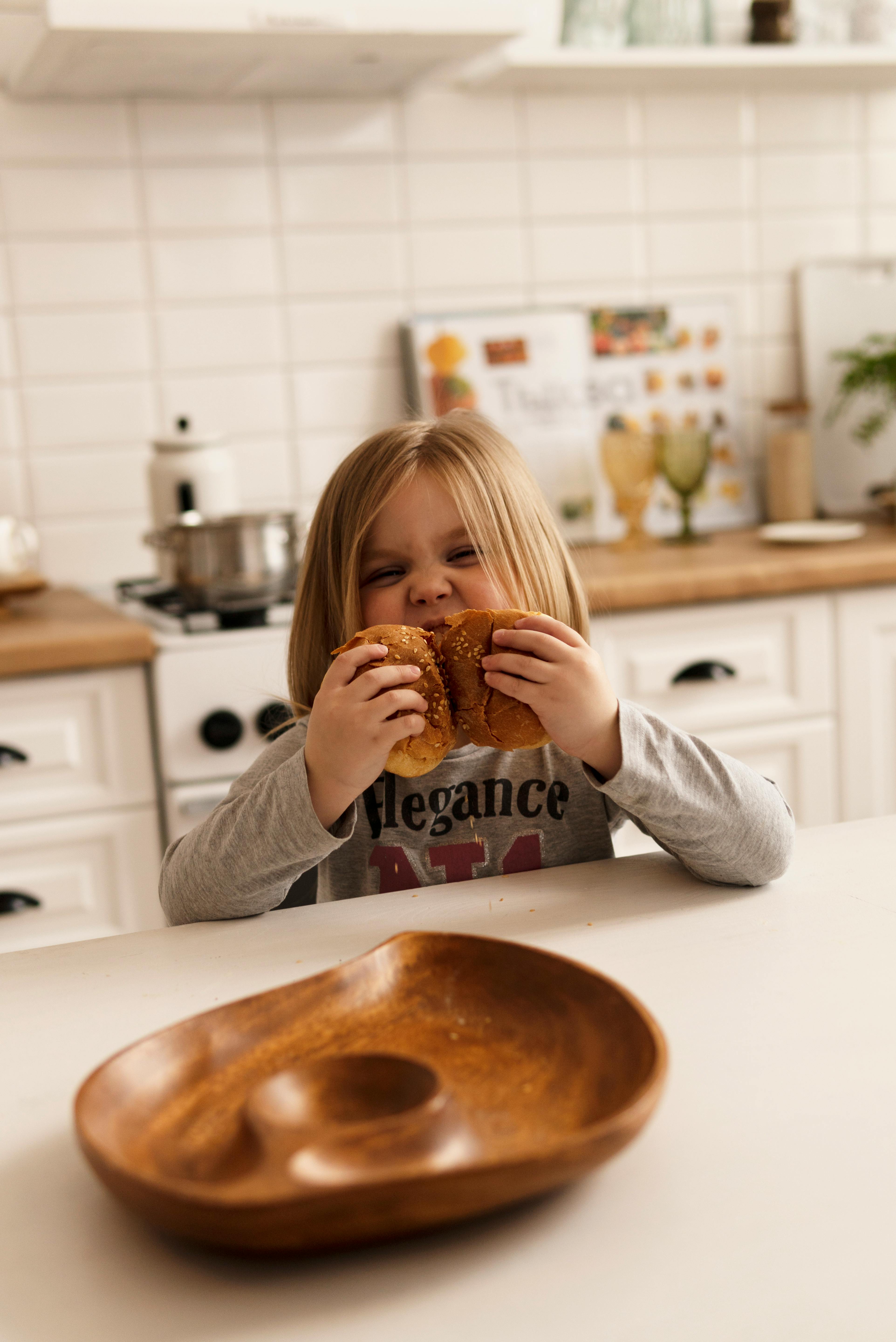 Little Girl Eating Burger In Kitchen