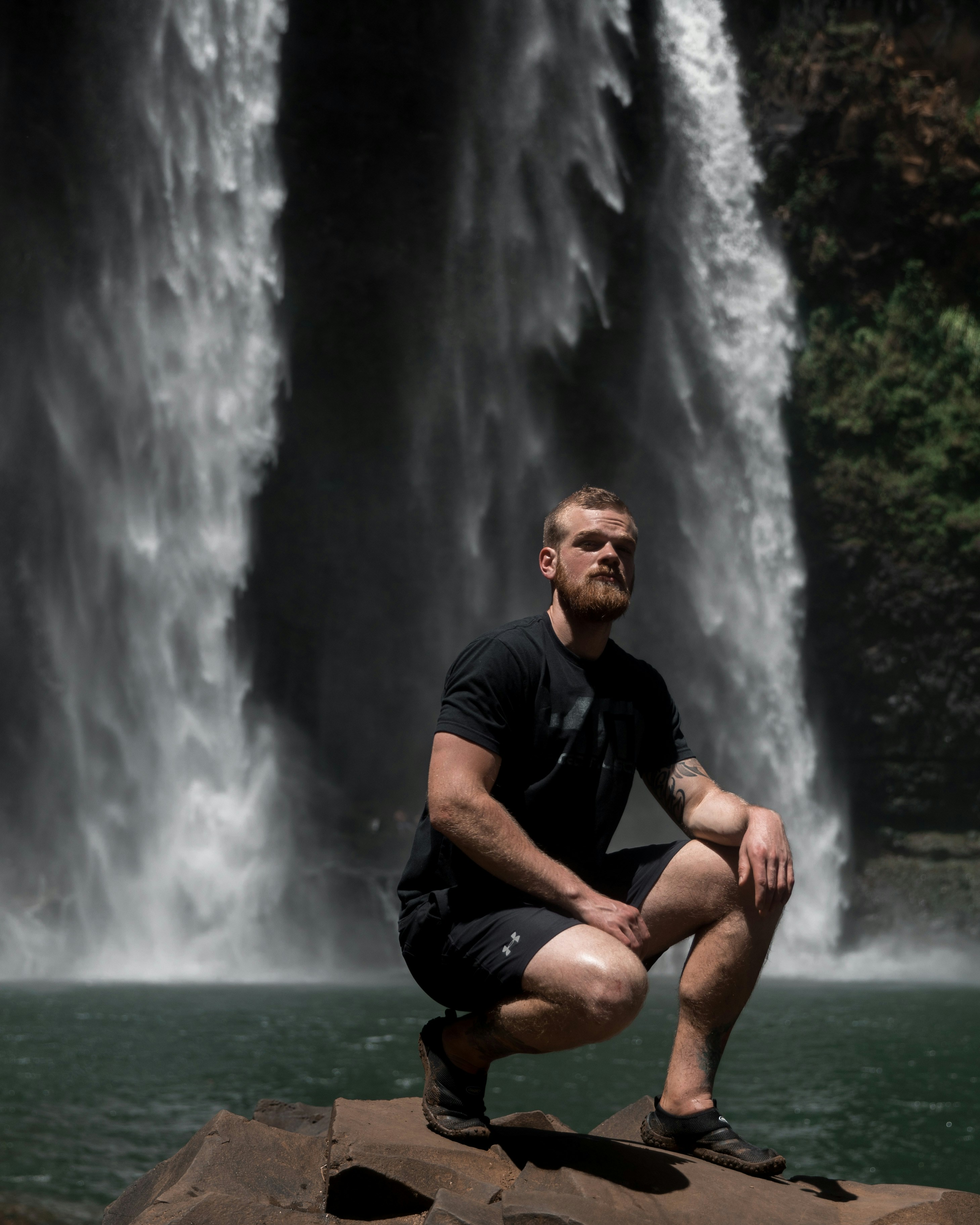 Man Crouching Before Large Waterfall